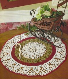 a crocheted doily with a basket and candy cane on the table next to it