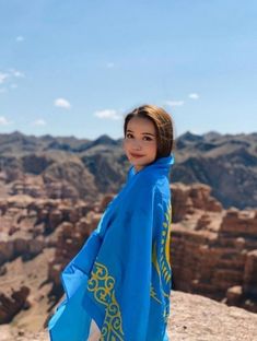 a woman standing on top of a mountain wearing a blue and yellow shawl with mountains in the background