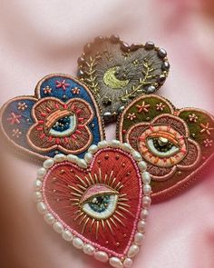 three heart shaped brooches with eyeballs and pearls on pink silk material background