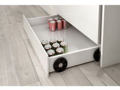 an open drawer with six cans of soda in it on the floor next to a wall