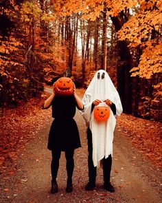 two people dressed up as ghost and pumpkins walking down a path in the woods