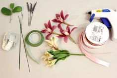 flowers, tape and scissors are laid out on a white surface with some green leaves