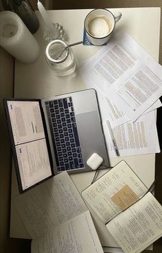 an open laptop computer sitting on top of a desk next to papers and cups of coffee