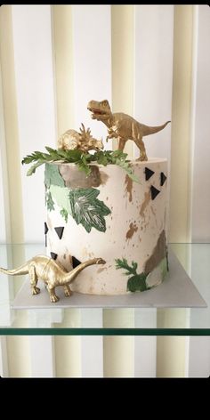 there is a cake decorated with dinosaurs and plants on the top shelf in front of striped wallpaper