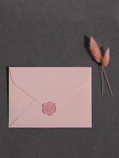 a pink envelope with a wax stamp on it next to a flower and a pair of scissors