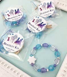 three bracelet kits in plastic bags on a table next to a white frame and blue glass beads