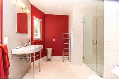 a bathroom with red walls and white tile flooring, along with a walk in shower