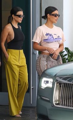 two women in matching outfits are walking out of a building with one woman carrying a purse