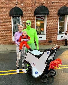 two people in alien costumes are pushing a stroller with a child on it and an adult standing next to them