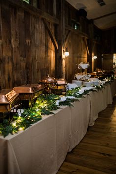 a long table is set up with white linens and greenery on the tables