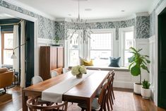 a dining room table and chairs in front of a window with floral wallpaper on the walls