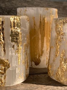 three gold and white vases sitting on top of a wooden table next to each other