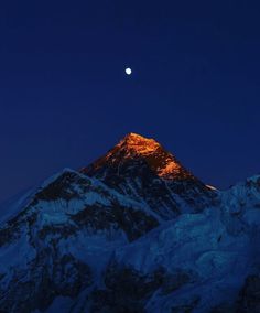 the moon is setting on top of a snowy mountain with snow covered mountains in the foreground