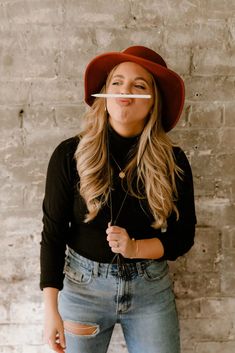 a woman wearing jeans and a red hat poses for the camera while holding an object in her mouth