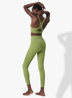 a woman in a green sports bra top and leggings with her hands on her head