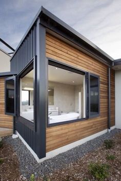 a modern house with wood siding and glass windows on the outside, along with gravel ground