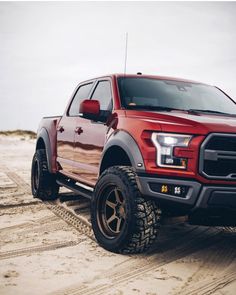 a red truck parked on top of a sandy beach