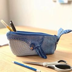 a pair of scissors and pencils are in a denim pouch on a table next to some pens