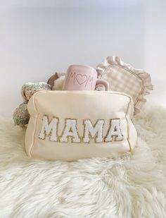 a white purse with the word mama on it sitting on top of a pile of pillows