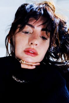 a close up of a person wearing a black shirt and holding her hand to her face