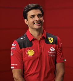 a man wearing a red shirt and black pants smiles while standing in front of a red wall