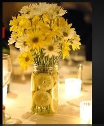 a mason jar filled with lemons and daisies sitting on a dining room table