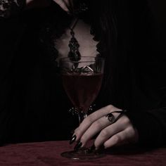 a woman sitting at a table with a wine glass in front of her and holding a drink