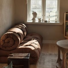 a couch sitting in front of a window next to a wooden table and book shelf