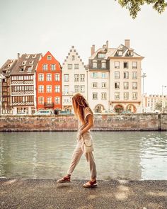 a woman walking along the water in front of some buildings