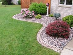 a garden with flowers and rocks in front of a brick fenced yard, along side a house