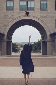 a woman is walking through an archway with her hand up in the air and she's wearing a graduation cap