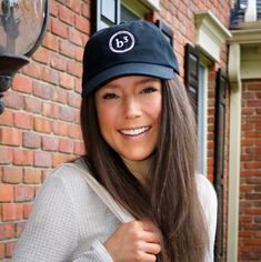 a woman with long hair wearing a hat and smiling at the camera while standing in front of a brick building