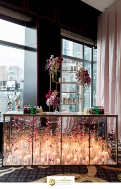 a buffet table with candles and flowers on it in front of a window overlooking the city