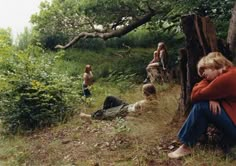 a group of people sitting on top of a grass covered hillside next to a forest