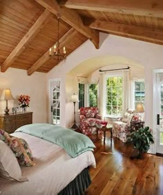 a bedroom with wood floors and white walls has a large bed, two chairs, windows, and a chandelier