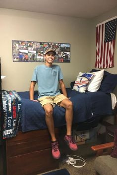 a man sitting on top of a bed in a room with an american flag hanging above it