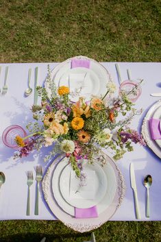 the table is set with plates, silverware and flowers