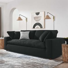 a living room with a black couch and two lamps on the wall, an art piece in the background