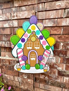 a gingerbread house with balloons and candy on the side of a brick wall in front of some flowers