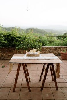 a wooden table sitting on top of a tiled floor next to a lush green hillside