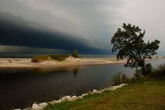 a large body of water sitting next to a lush green field under a cloudy sky