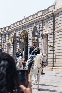 two men in uniform riding horses down the street with people taking pictures on their cell phones