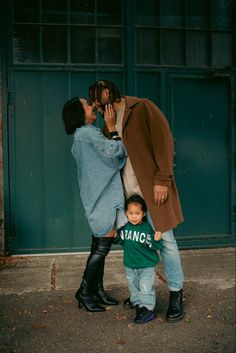 a woman, man and child standing in front of a green building with their hands on each other's heads