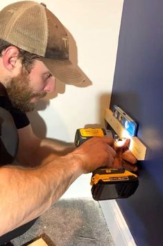 a man is working on a wall with a drill and some screwdrivers in his hand