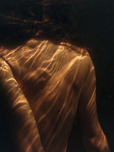 the back of a woman's body is reflected in water with sunlight coming through her hair