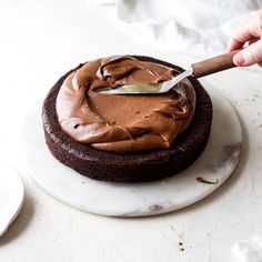 a person spreading chocolate frosting on top of a cake