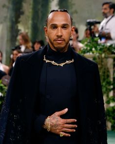 a man with his hands on his hips wearing a black suit and gold bracelets