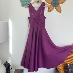 a purple dress hanging on a clothes rack in front of a wall with flowers attached to it