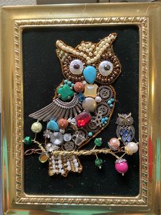 an owl with beads and jewels in a gold frame on a black background is shown