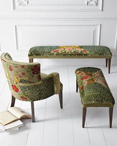 a living room with white floors and floral upholstered chairs, ottomans, and an open book on the floor